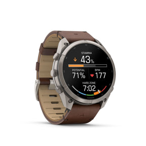 Garmin älykello harmaalla titaanikotelolla ja pähkinänruskealla nahkarannekkeella, pyöreä musta AMOLED-näyttö
