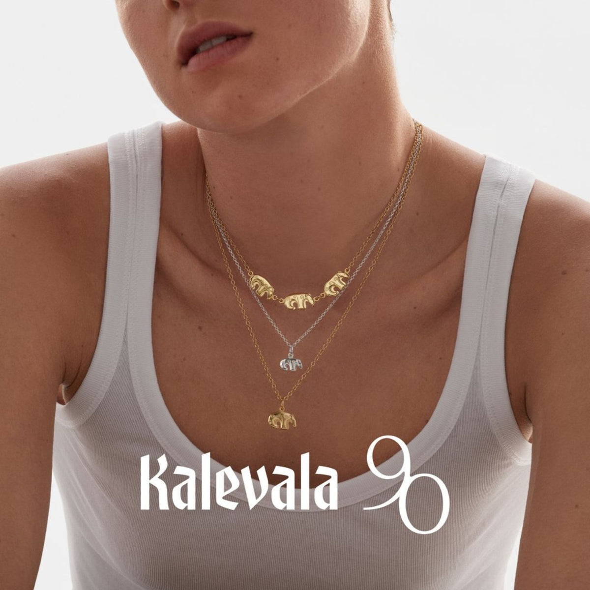 Kalevalan hopeinen karhuriipus mallin kaulassa valkoista toppia vasten, pieni karhuhahmo näkyy ketjussa rinnalla