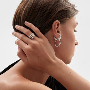 Kalevalan hopeinen ear cuff korvakoru naisen korvassa, sivuprofiilissa käsi hiuksilla ja hopeiset korurenkaat näkyvissä