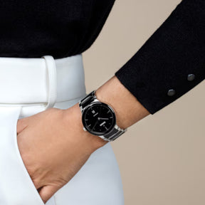 Rado automaattinen rannekello mustalla kellotaululla ja teräksenvärisellä rannekkeella ranteessa tumman bleiserin kanssa