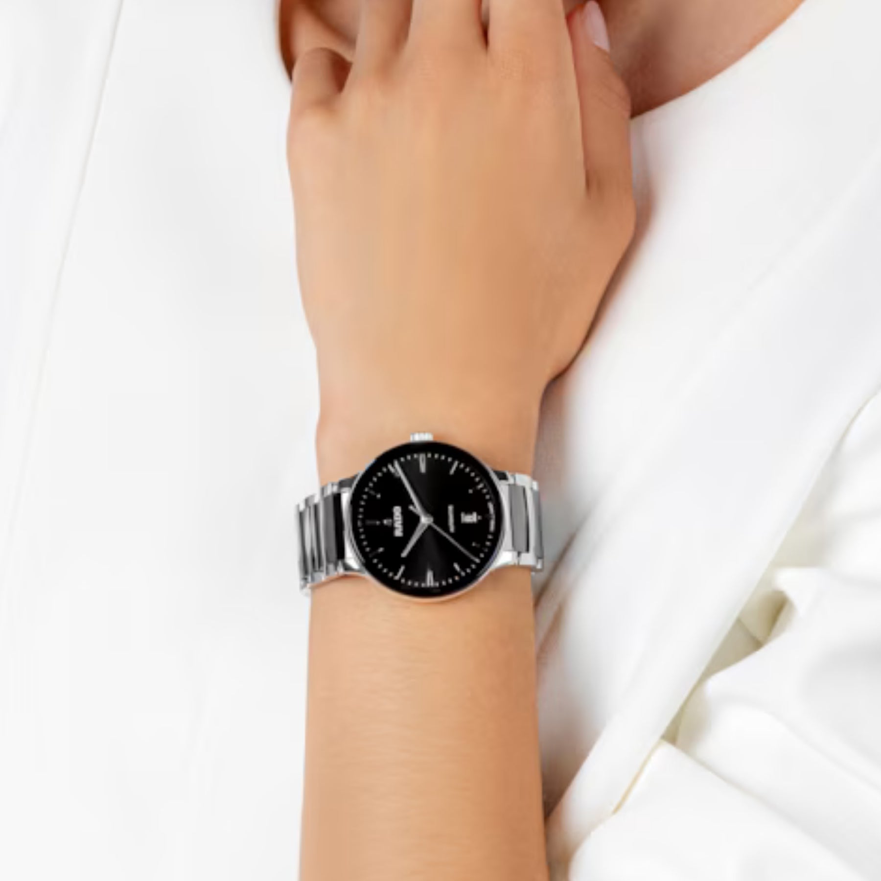Rado rannekello mustalla kellotaululla ja teräksenvärisellä rannekkeella ranteessa pukeutumisen yhteydessä