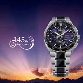 Seiko Astron -rannekello tummalla kronografitaululla ja teräsrannekkeella, 145-vuotisjuhlagrafiikka auringonlaskussa