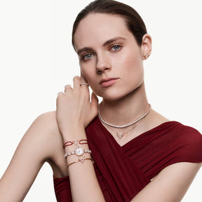 Swarovski-koruja esittelevä nainen punaisessa asussa, kaulakorut, rannekorut, korvakorut ja sormukset näkyvissä