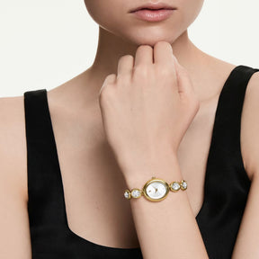 Swarovski-rannekello naisen ranteessa, keltakullattu ovaali kuori, kristallikoristeinen taulu ja kristalliranneke